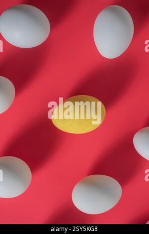 A bright conceptual image showing a yellow egg standing out from the white eggs on a vibrant red background. Stock Photo
