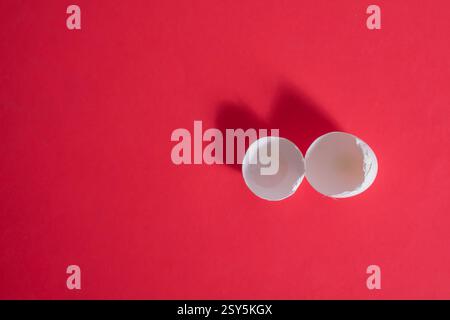 Two empty eggshell halves are set against a vibrant red surface, casting soft shadows Stock Photo