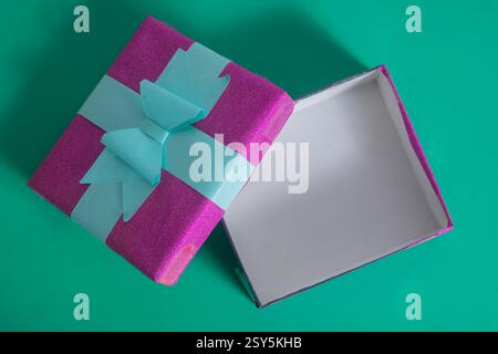An elegant open pink gift box decorated with a blue ribbon on a vivid green background, surprise, and festive moments. Stock Photo