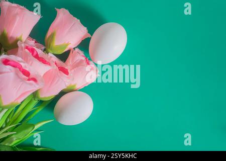 A composition of pink flowers and white eggs on a vibrant green background with copy space for text. Stock Photo