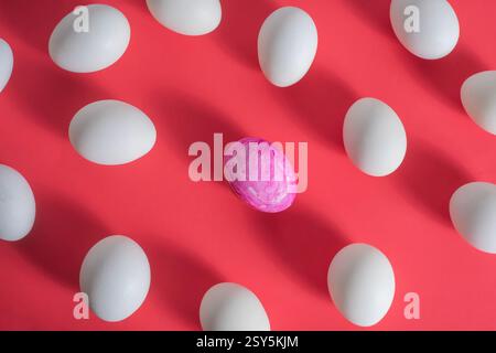 A unique pink egg amidst a pattern of white eggs on a vibrant red background. Stock Photo