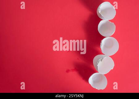 Five broken eggshells artistically placed on a red surface, creating an abstract and minimalist composition. Stock Photo