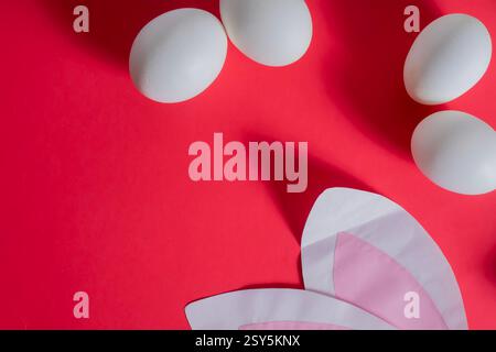 A collection of white eggs and paper bunny ears on a vibrant red background that evokes Easter. Stock Photo
