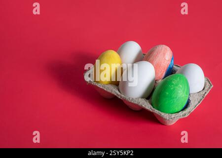 Vibrant Easter eggs are placed in a cardboard box and displayed on a vibrant red background. Perfect for themes of celebration, holidays and creativit Stock Photo
