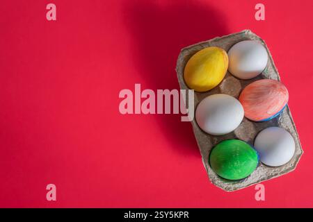 Vibrant Easter eggs are placed in a cardboard box and displayed on a vibrant red background. Perfect for themes of celebration, holidays and creativit Stock Photo