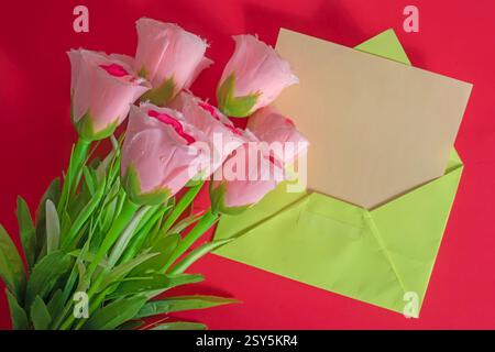 A bouquet of pink roses placed next to a green envelope with a red background evokes love, appreciation, or celebration. Stock Photo