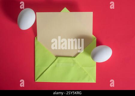 A colorful composition with a green envelope, beige paper, and two white eggs resting on a red surface. Stock Photo