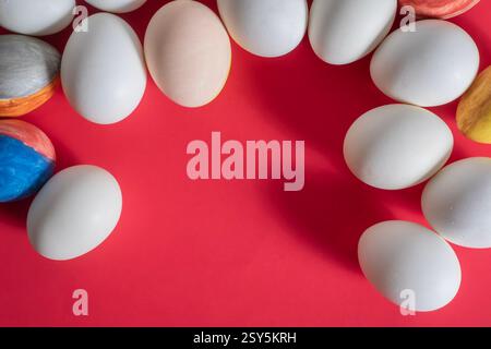 Easter eggs of various colors, including plain white and beautifully painted ones, are set against a vibrant red background. Stock Photo