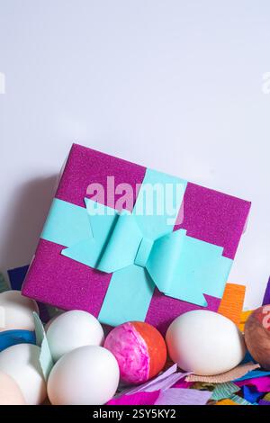 A vibrant gift box adorned with blue ribbon, surrounded by eggs and colorful decorations. perfect for events like Easter, birthdays, or parties. Stock Photo