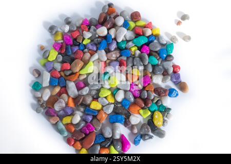 Brightly colored pebbles are stacked on a plain white surface, showing off a vibrant assortment. Stock Photo