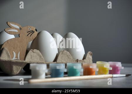easter holidays DIY painting concept. Eggs, colorful paints, brush and white eggs in paper holder, box. White background, place for the copy Stock Photo