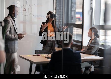 Business professionals in a modern office discussing artificial intelligence. A woman wearing a VR headset presents ideas while colleagues listen Stock Photo