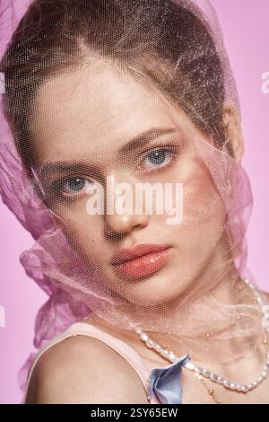 A stunning young woman with captivating features poses gracefully against a soft pink background. Stock Photo