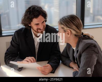 Two well-dressed business professionals having an engaged discussion over documents and a laptop in a modern office setting, collaborating on a busine Stock Photo
