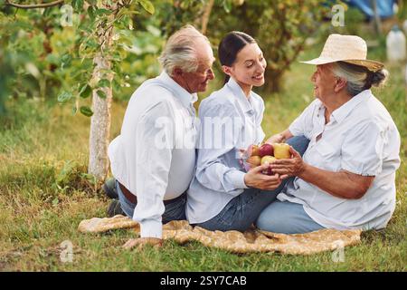 With apples. Sitting on the ground. Daughter is with her senior mother and father is in the garden. Stock Photo
