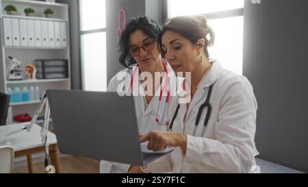 Two women doctors discussing patient data on a laptop in a hospital room showcasing workplace collaboration and clinical expertise indoors. Stock Photo