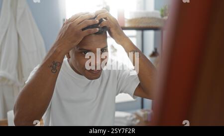 Young hispanic man in a spa room examining his hair in the mirror with a focused expression on his face Stock Photo