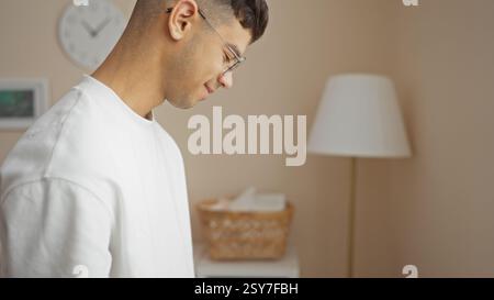 Young man in profile standing indoors in a cozy living room setting, conveying a warm, inviting, and stylish atmosphere with soft lighting. Stock Photo