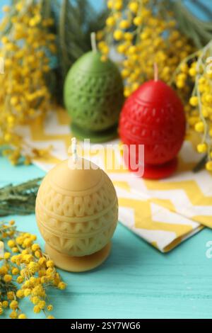 Colorful egg-shaped candles and mimosa flowers on turquoise wooden table, closeup. Easter decor Stock Photo