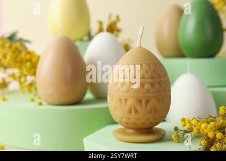 Beautiful egg shaped candles and mimosa flowers on beige background, closeup. Easter decor Stock Photo