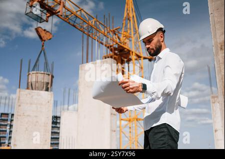With plan in hands. Man in uniform is working on the construction site. Stock Photo