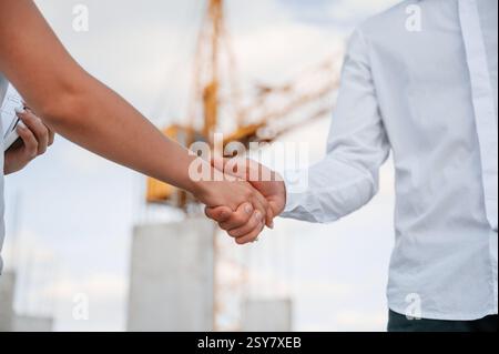 Close up view. Doing handshake. Man in uniform working with woman on the construction site. Stock Photo