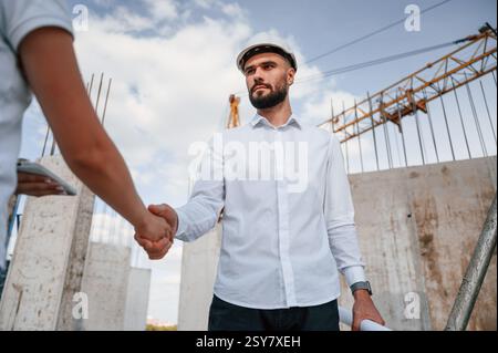Doing handshake. Successful agreement. Man in uniform working with woman on the construction site. Stock Photo