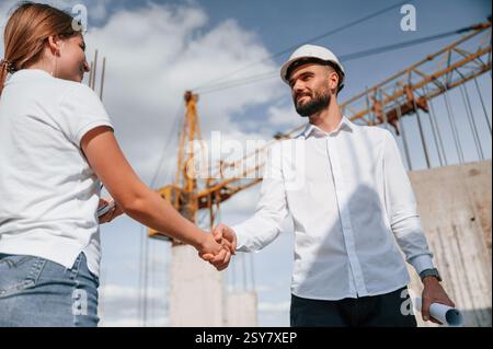 Doing handshake. Successful agreement. Man in uniform working with woman on the construction site. Stock Photo