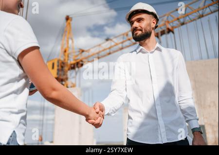 Doing handshake. Successful agreement. Man in uniform working with woman on the construction site. Stock Photo