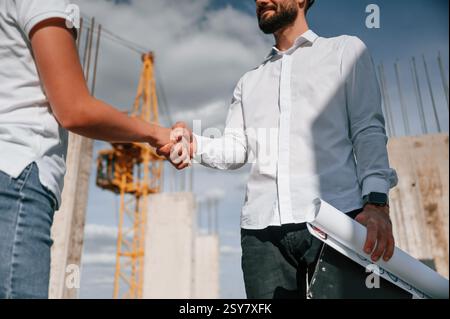 Doing handshake. Successful agreement. Man in uniform working with woman on the construction site. Stock Photo