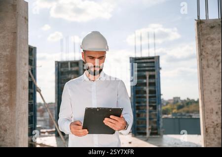 With notepad with documents. Foreman in uniform is working on the construction site. Stock Photo