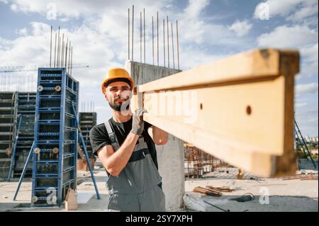Carrying wooden plank. Man in uniform is working on the construction site. Stock Photo