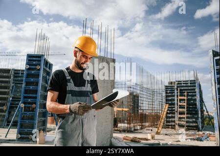 Control of the process. Foreman is with documents. Man in uniform is working on the construction site. Stock Photo