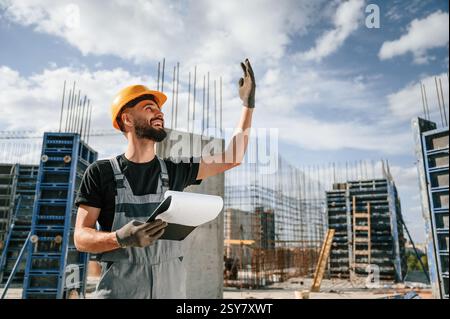 Control of the process. Foreman is with documents. Man in uniform is working on the construction site. Stock Photo