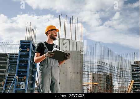 In hard hat, with notepad. Man in uniform is working on the construction site. Stock Photo