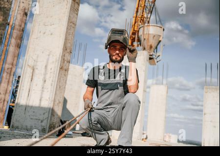 In welding mask. Man in uniform is working on the construction site. Stock Photo