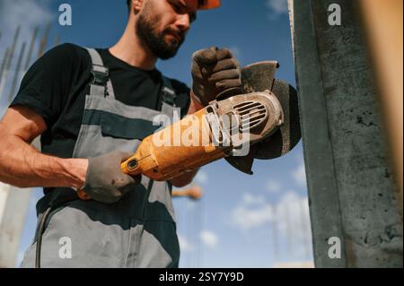 Holding grinding machine. Man in uniform is working on the construction site. Stock Photo