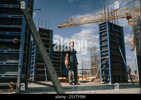 Standing with grinding machine in hands. Man in uniform is working on the construction site. Stock Photo