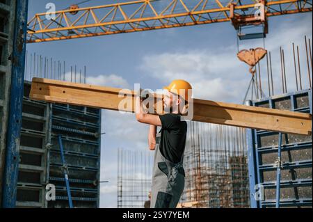Against crane with wooden plank. Man in uniform is working on the construction site. Stock Photo