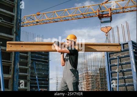 Against crane with wooden plank. Man in uniform is working on the construction site. Stock Photo