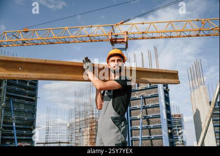 Against crane with wooden plank. Man in uniform is working on the construction site. Stock Photo