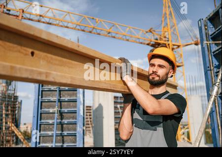 Against crane with wooden plank. Man in uniform is working on the construction site. Stock Photo