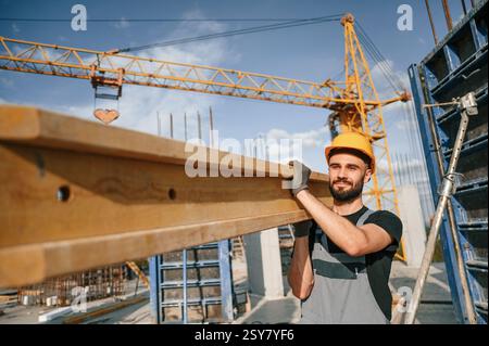 Against crane with wooden plank. Man in uniform is working on the construction site. Stock Photo