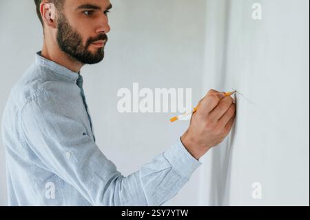 Doing marks by pencil on the wall. The man is making repairs in the apartment. Stock Photo