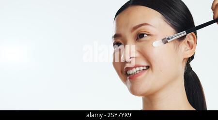 Asian woman, face and brush cream for beauty, aesthetic skincare and mockup white background. Happy studio model, makeup and facial lotion for Stock Photo
