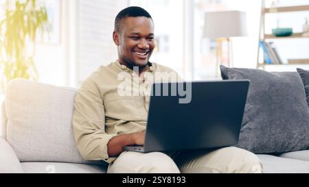 Laptop, sofa and happy black man typing in living room, working or social media in house. Freelancer, remote worker and person with computer on couch Stock Photo