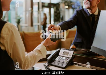 Back view of female receptionist holding wireless payment terminal while hotel guest tapping card Stock Photo