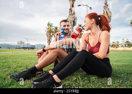 Happy couple enjoying refreshing drinks while taking a break from their energetic workout in the sunny park, smiling and laughing together, promoting a healthy lifestyle and fitness motivation. High quality photo Stock Photo