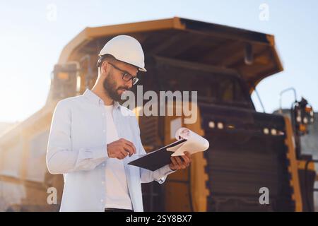 In glasses, reading documents. Man in uniform is working in the quarry at daytime. Stock Photo