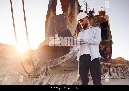 Using laptop. Man in uniform is working in the quarry at daytime. Stock Photo